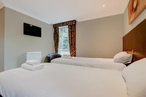 A hotel room with two beds, a flat-screen TV mounted on the wall, a window with patterned curtains, and a radiator. - Standard family of 5 room (Liverpool)