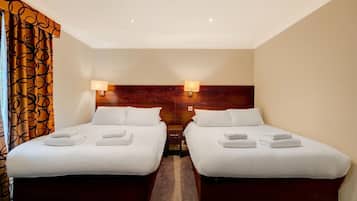 A hotel room with two beds, each with white linens and towels, a wooden headboard, and two wall-mounted lamps.