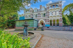 A historic building with a fountain, a sign indicating it's the Liverpool Aigburth Hotel, and a paved walkway.