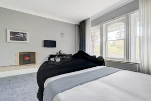 Een slaapkamer met een groot bed, een open haard, een televisie en een raam met gordijnen.