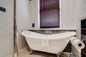 A bathroom with a freestanding bathtub, a toilet, and a window with blinds.