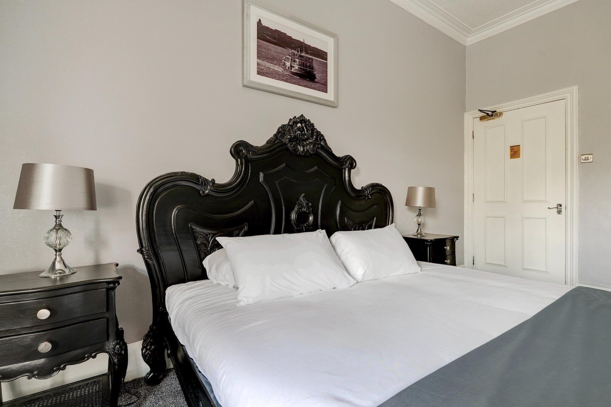 A neatly made bed with white linens in a room with a classic black headboard.