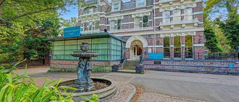 A historic building with a fountain, a sign indicating it's the Liverpool Aigburth Hotel, and a paved walkway.
