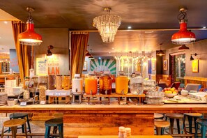 Een bar met een houten toonbank, diverse drankdispensers en hangende lampen.