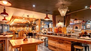Een restaurantinterieur met houten tafels, een bar en hangende lampen.