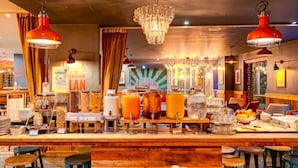Una zona de bar con mostrador de madera, varios dispensadores de bebidas y luces colgantes.