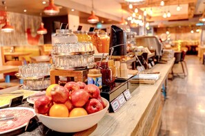 Un espace buffet proposant une variété d'aliments et de boissons, notamment des pommes, des oranges et des pots de condiments.