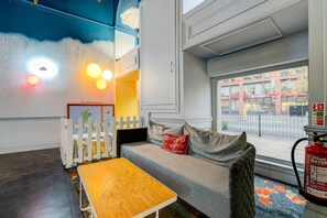 Une pièce chaleureuse avec une table en bois, un canapé gris agrémenté de coussins rouges, une clôture blanche en bois et une fenêtre donnant sur l’extérieur.
