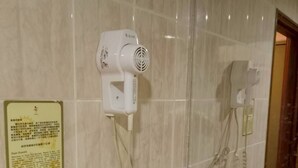 Un bagno con asciugacapelli montato a parete, un telefono e uno specchio che riflette l'ambiente.