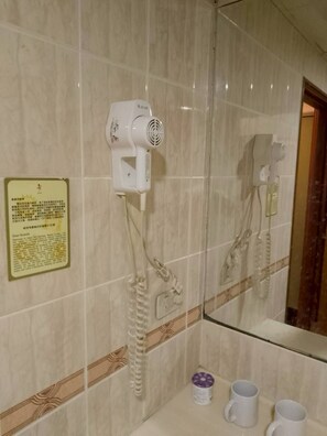 A bathroom with a hairdryer mounted on the wall, a telephone, and a mirror reflecting the room.