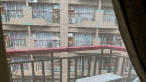Un balcone con tavolo e sedie, ringhiera in rete e vista sui palazzi circostanti.