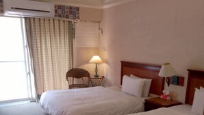 Una camera d'albergo con due letti, una sedia, una lampada e un condizionatore d'aria.