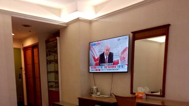 Una camera d'albergo con due letti, una scrivania, un televisore e uno specchio.