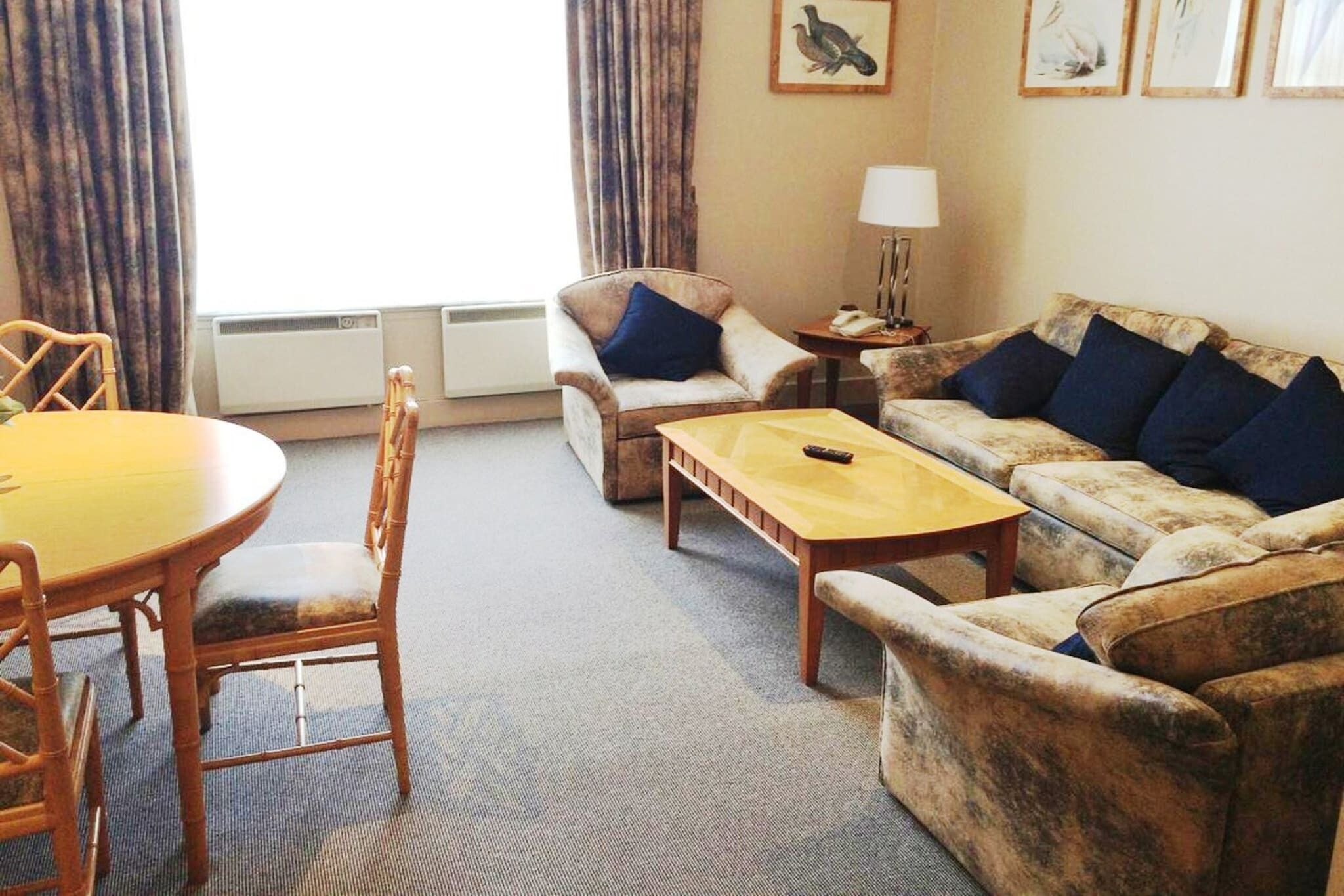 A living room with a round table, two armchairs, a sofa, a lamp, and a framed picture on the wall.