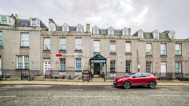 A multi-story hotel with a prominent entrance, a red car parked in front, and a clear sky. - Brentwood Aberdeen City Centre - Standard Twin Room (Aberdeen)