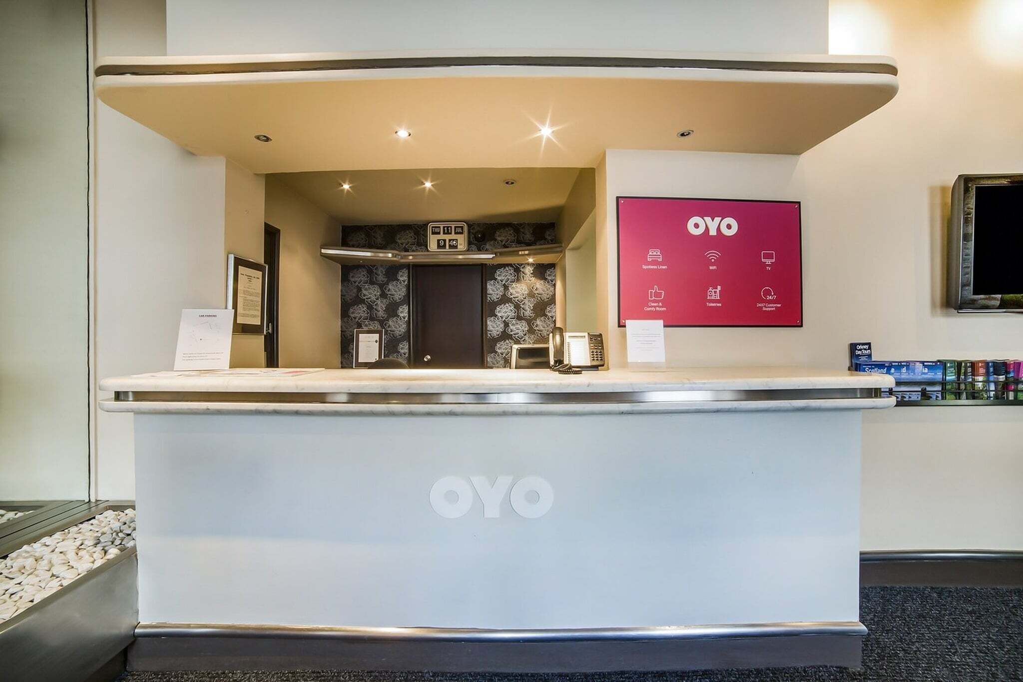 A reception desk with the OYO logo, a digital display, and a framed certificate on the wall.