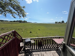 A wooden deck with a barbecue grill, overlooking a grassy field and a body of water. - Horns Skärgårdscamping (Nyköping)