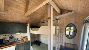Una cabaña acogedora con kitchenette, camas literas y una pequeña zona de estar.