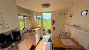 Cocina compacta con ventana, mesa de comedor con sillas y vista a un campo verde.