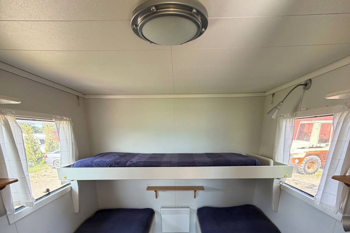 A compact interior with two single beds, a small table, and a ceiling light fixture.