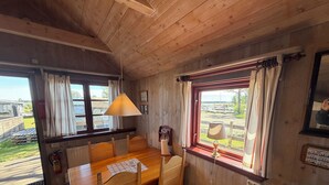 Un interior de madera con una mesa de comedor, sillas, una ventana con cortinas y vistas al exterior.