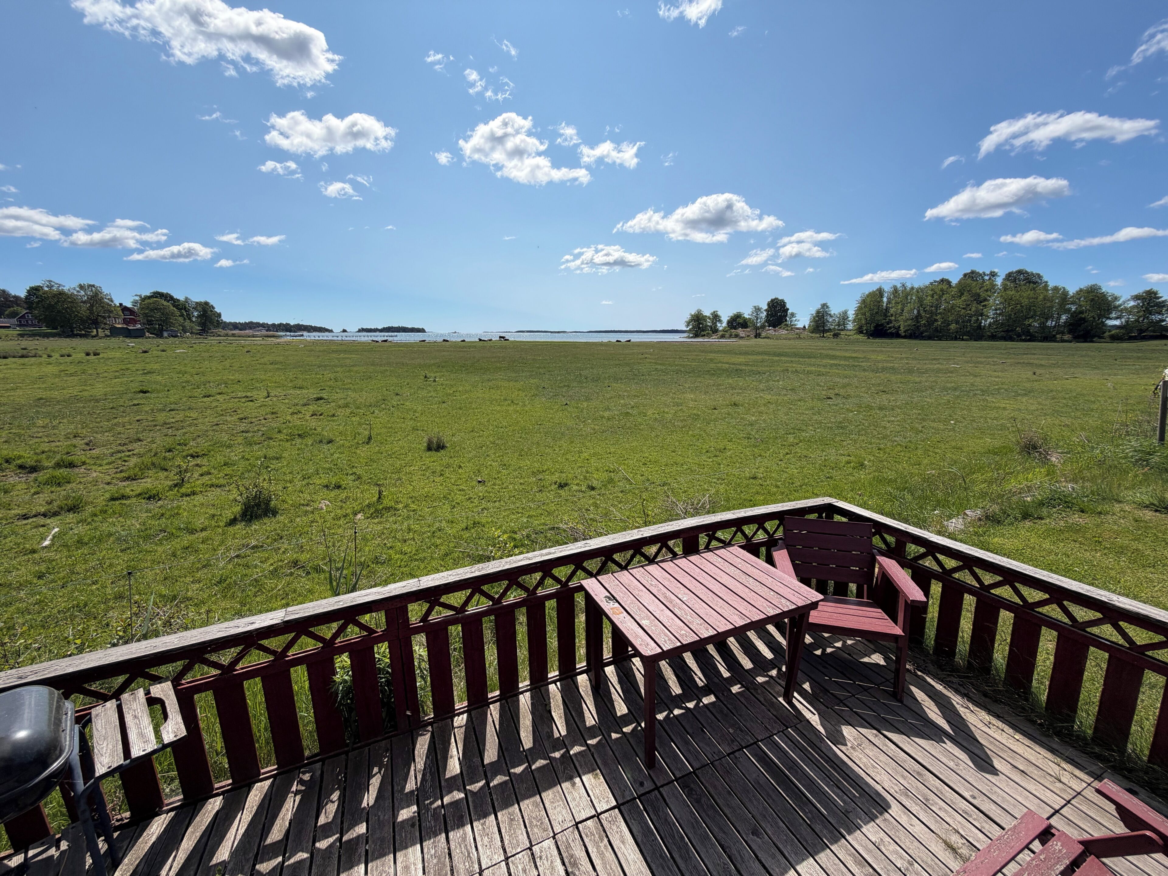 A wooden deck with a table and chairs, overlooking a grassy field and a body of water.
