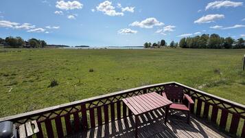 A wooden deck with a table and chairs, overlooking a grassy field and a body of water.