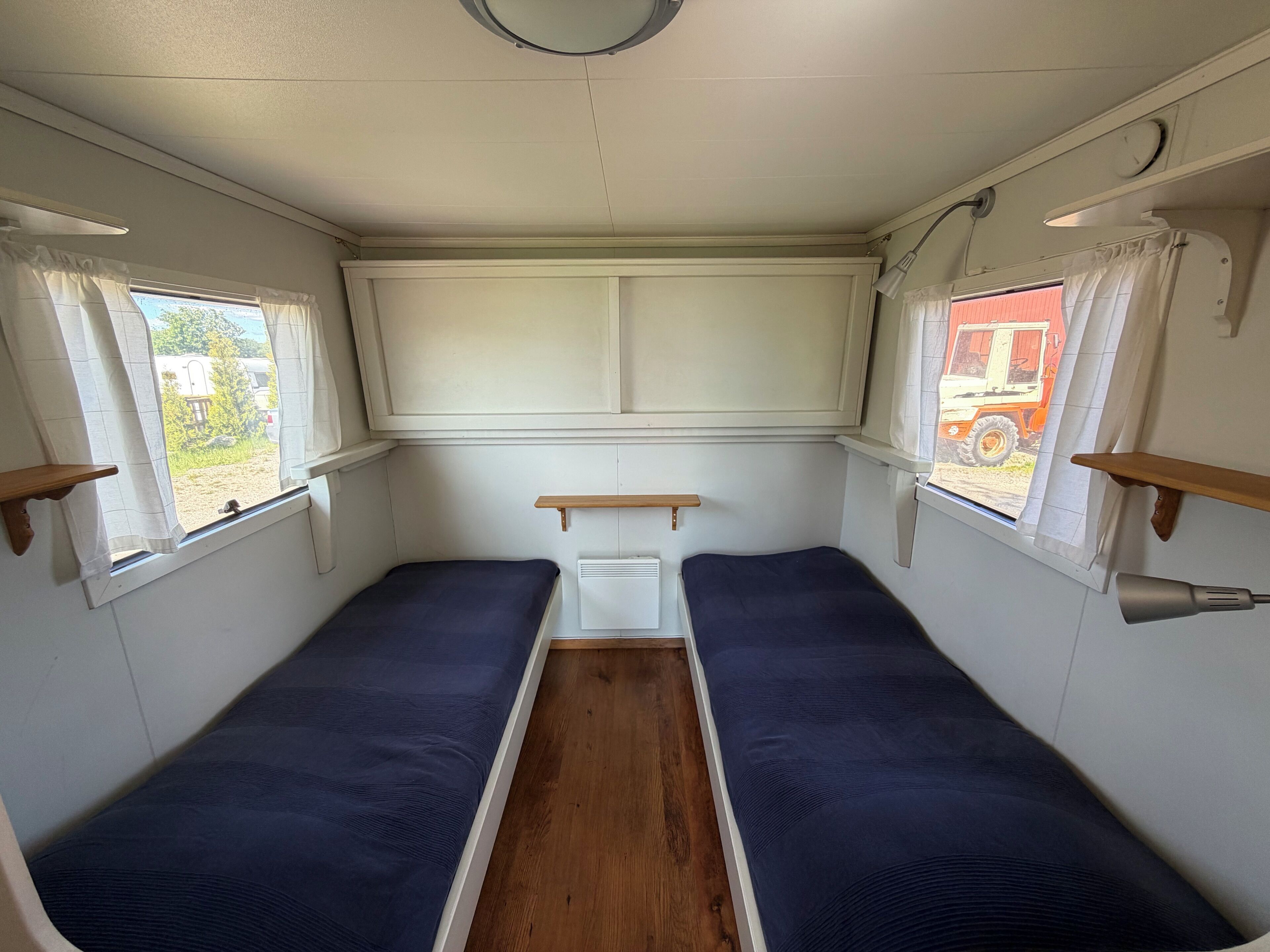 A compact interior with two single beds, a small table, and a window with curtains.