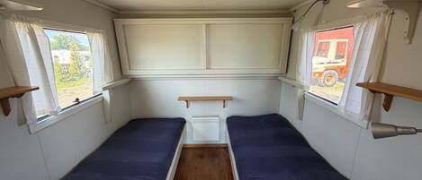A compact interior with two single beds, a small table, and a window with curtains.