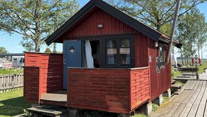Una cabaña de madera pequeña y roja con un balcón, una ventana y una puerta.