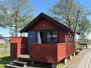 A small red wooden cabin with a balcony, a window, and a door. - Horns Skärgårdscamping (Nyköping)