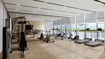 A modern gym with various exercise equipment, large windows, and a wooden floor.