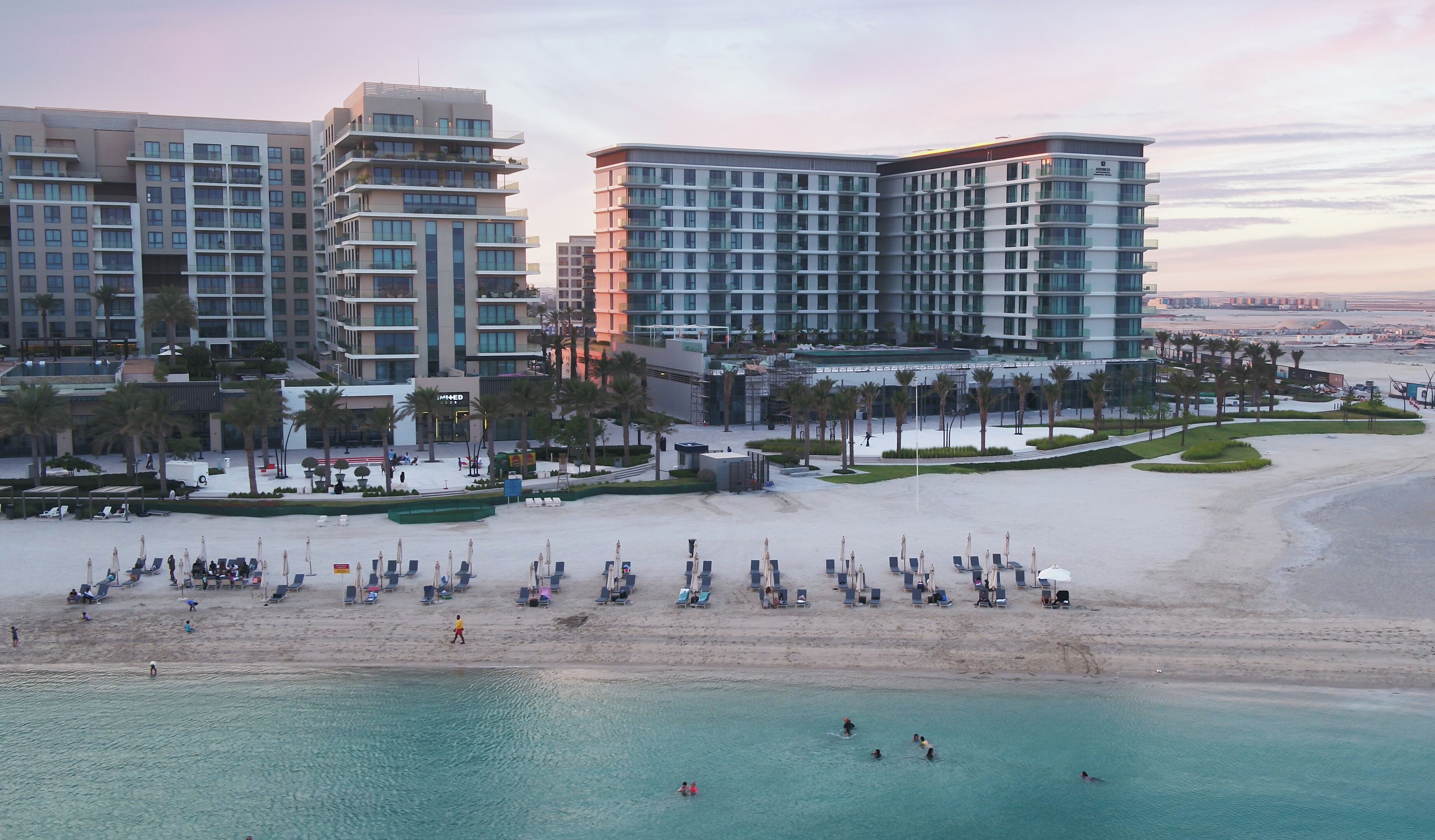 Un hotel costero con varios edificios altos, una playa arenosa con tumbonas y una vista despejada del mar.