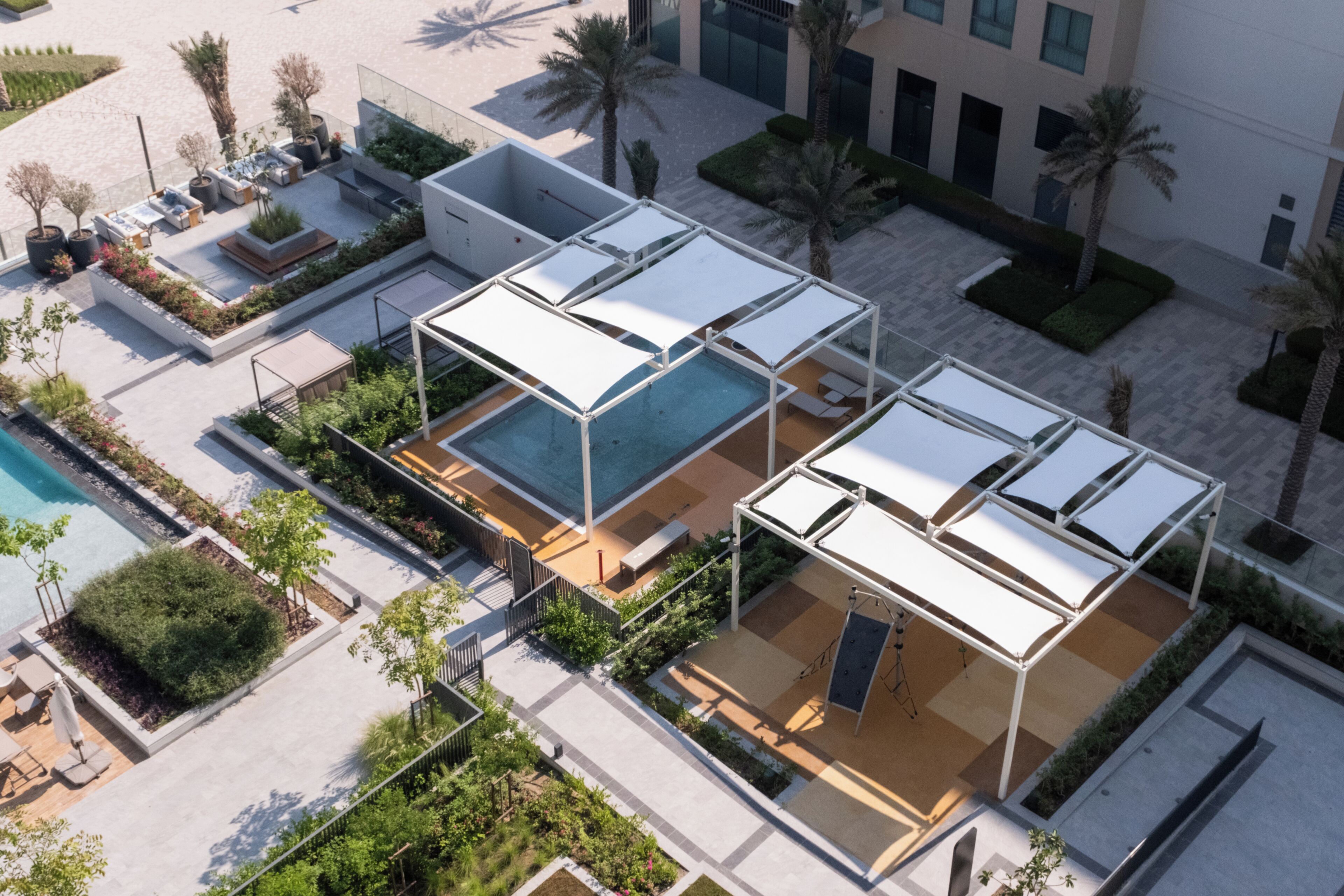 A rooftop pool area with sun loungers and a swimming pool, surrounded by greenery and palm trees.