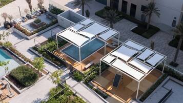 A rooftop pool area with sun loungers and a swimming pool, surrounded by greenery and palm trees.