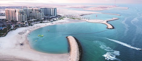 Vista aérea de una zona costera con playa, puerto deportivo y un complejo hotelero.