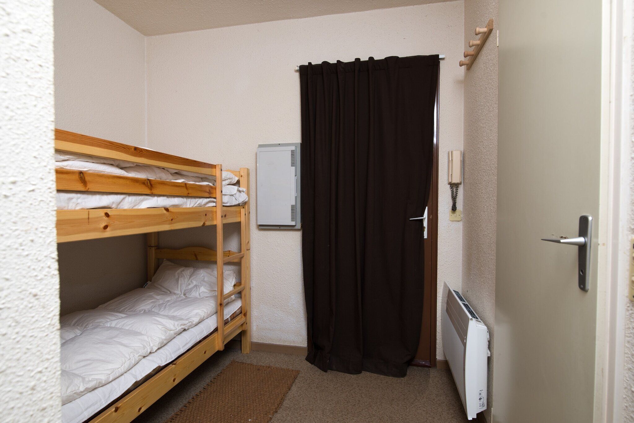 A small, compact room with bunk beds, a radiator, a door, and a wall-mounted heater.