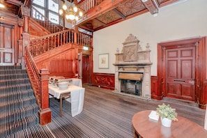 Una imponente escalera que conduce a un nivel superior, una chimenea con repisa y una mesa dispuesta para comer.