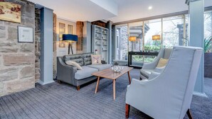A modern living room with a grey sofa, a white armchair, a wooden coffee table, and a bookshelf. - Deluxe Family studio (Dundee)