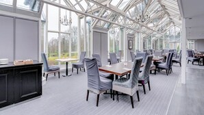 A spacious room with a high ceiling and large windows, featuring a modern dining setup with tables and chairs. - Deluxe Family studio (Dundee)