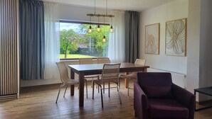 Ruokailutilassa on puinen pöytä ja tuolit, violetti nojatuoli sekä taideteoksia seinällä.