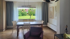 Ruokailutila, jossa on pöytä ja tuolit, violetti nojatuoli ja ikkunasta avautuva näkymä puutarhaan.