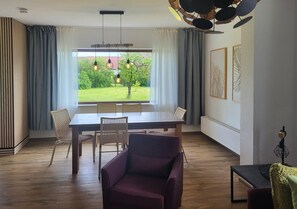 Un coin repas avec une table et des chaises, un fauteuil violet et une vue sur un jardin par la fenêtre.