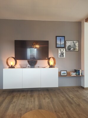 Un salon moderne doté d’un téléviseur à écran plat, de deux lampes fixées au mur, d’un vase décoratif et de tableaux encadrés accrochés au mur.