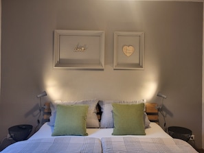 A bed with patterned bedding, two pillows, a bedside table, and two wall-mounted lamps.