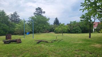 A grassy outdoor area with a swing set, trees, and a building in the background.