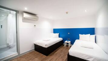 Habitación de hotel con dos camas, cabina de ducha de vidrio y una mesita de noche pequeña.