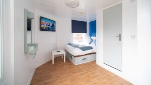 Ein Schlafzimmer mit einem Bett, einem kleinen Tisch, einem Spiegel, einem Gemälde und einer Tür.