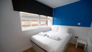 Ein Schlafzimmer mit Bett, Fenster, einem kleinen Nachttisch und einer blauen Akzentwand.