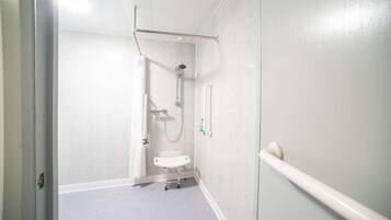 En smal hall med en duschhörna, en vit bänk och ett handräcke på höger sida.